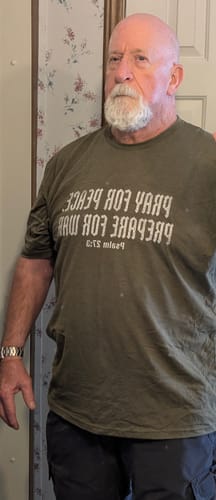 Reviewer wearing an olive green t-shirt with Christian text that says Pray for peace, prepare for war.