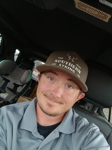Customer's Hat of the Month Crew hat, a brown cap with Southern String branding, worn by a reviewer in a car.