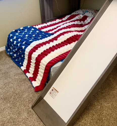 Customer's Hugs Flag Blanket with a red, white, and blue patriotic design spread across a bed with a slide.