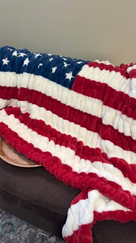 Customer's Hugs Flag Blanket with a plush, red, white, and blue American flag pattern draped over a sofa.