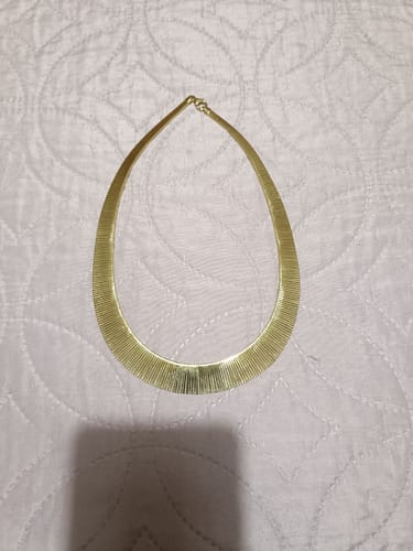 Customer's gold-colored Collana Cleopatra laid flat against a textured white background.