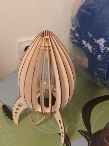 Customer's Ariane lampe baladeuse en bois en forme de fusée posée sur une table près d'un globe terrestre.