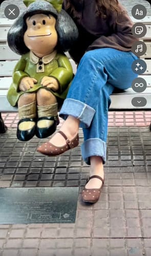 Customer's Zapato Ballerina Suede Café Tachas worn by a person sitting on a bench next to a statue.