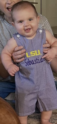Customer's baby wearing a personalized purple gingham LSU Jon Jon outfit held by an adult.