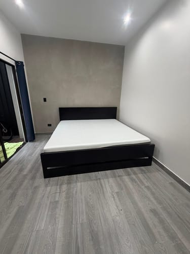 Customer's Colchón Ortopédico Clásico, a white mattress placed on a black frame in a minimalist bedroom.