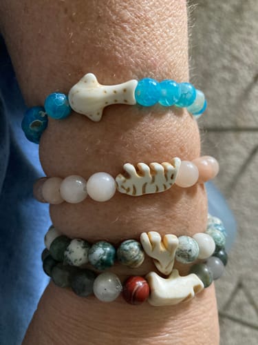 Reviewer's arm wearing four stacked The Quest bracelets with unique animal charms and colorful beads.