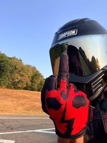 Customer's red OG MX Gloves worn by a person in a motorcycle helmet, pointing a finger on an outdoor road.