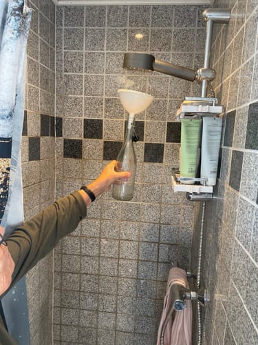 Anmelderens PureNordic brusehoved monteret i bruseniche, mens en hånd holder en tragt til en glasflaske.