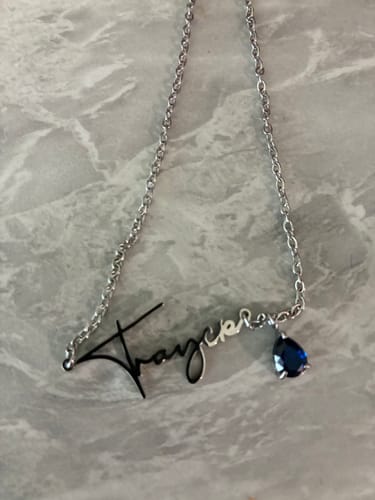 Customer's Lucce Signature Necklace featuring a personalized script name pendant and a blue teardrop stone charm.