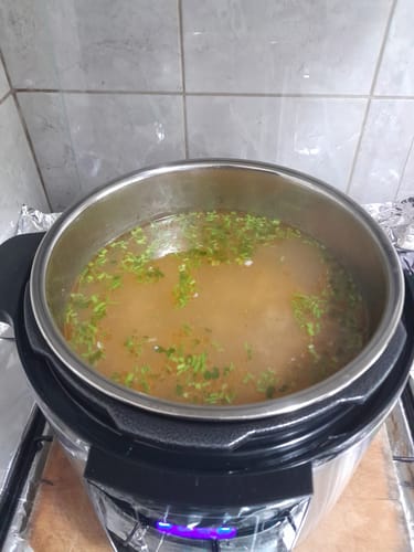 Customer's Novio SteelCook multicooker with the lid open, filled with a hearty broth and fresh green herbs.