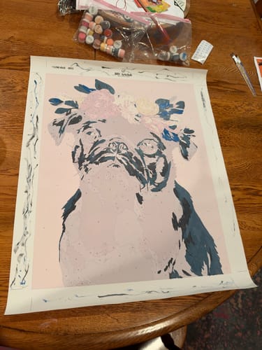 Customer's Surprise Painting by Numbers canvas of a pug wearing a floral crown, with paint pots on a table.