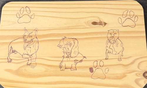 Customer's wooden board showing three burned dog portraits and paw prints created with the Creator Toolkit.