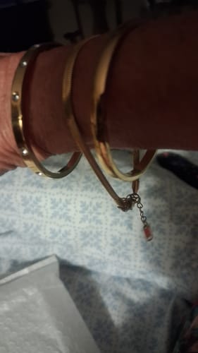 Customer's gold Chelsea Herringbone Bracelet worn on wrist alongside other bracelets, close-up.