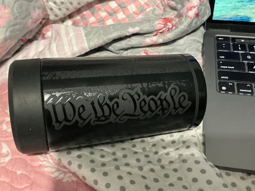 Customer's black We The People branded Universal Buddy can cooler next to a laptop on a patterned bedspread.