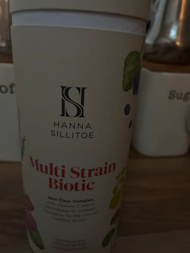 Customer's Multi Strain Biotic bottle, featuring brand logo and ingredient text, standing on a wooden surface.