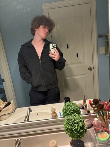 Customer's Batman Armored Zip-Up jacket in washed black, worn by a person taking a mirror selfie in a bathroom.