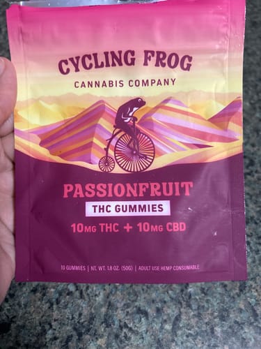 Customer's hand holding a pink and purple Cycling Frog Passionfruit THC gummy pouch.