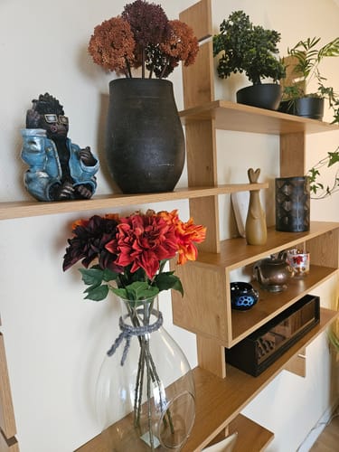Customer's Rockeape figur antikkgull plassert på en hylle sammen med blomstervaser og grønne planter.