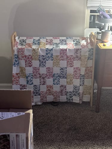Customer's unfinished Brick Prairie Precut Quilt Kit draped over a wooden stand, showing rows of floral and white bricks.
