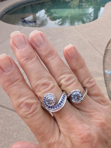 Customer's hand wearing two silver rings, one with blue sapphire accents and a grey center stone.