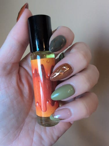 Reviewer's hand holding a Mad Honey roll-on perfume bottle with an orange label and dark cap.
