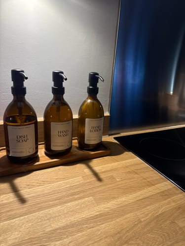 Customer's set of three amber glass bottles with metal pumps on a long wooden tray in a kitchen.