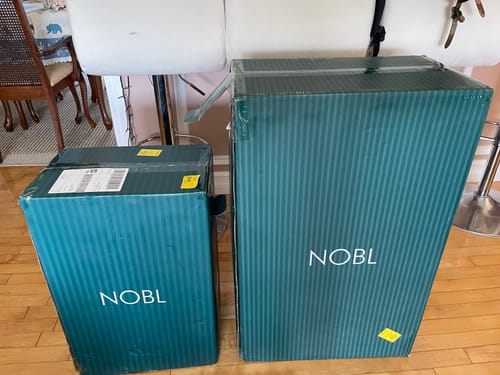 Reviewer's two green NOBL boxes on a hardwood floor, ready for unboxing.