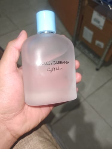 Customer's hand holding a frosted glass bottle of Dolce & Gabbana Light Blue Pour Homme perfume.