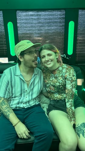 Reviewer wearing a tan Big Camp Hat, sitting next to a person in a green-lit space.