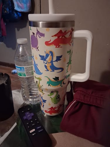 Customer's Cute Dragons CREWCUP with colorful dragon patterns, standing on a table next to a water bottle and remote.