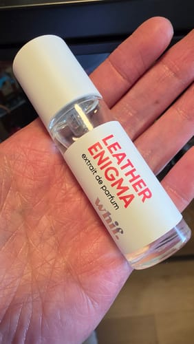 Reviewer's hand holding a small, clear glass bottle of Leather Enigma extrait de parfum with a white cap.