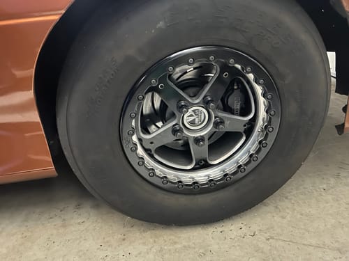 Reviewer's black lug nuts installed on a drag racing wheel with a large tire on an orange vehicle.