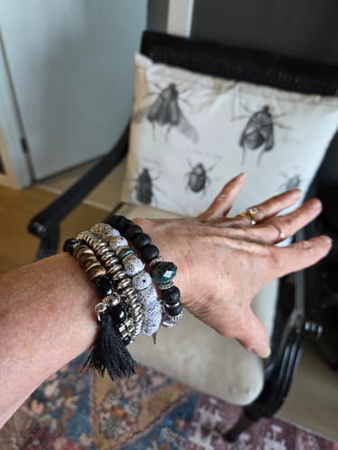 Customer's Michelle Stretchy Doodah Stack Bracelet worn on a hand, featuring black, white, and silver beads and a tassel.