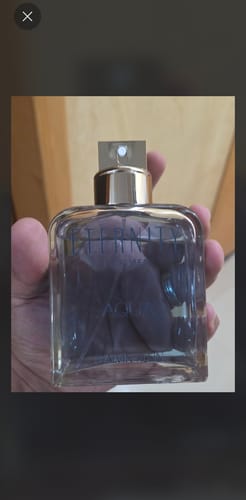 صورة العميل لزجاجة عطر كالفن كلاين إتيرنيتي أكوا للرجال الشفافة التي تمسكها يد، بتصميم أنيق وبسيط.