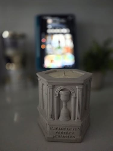 Customer's Deep Fall candle, shaped like a gray monument, sitting on a table with a blurred background.
