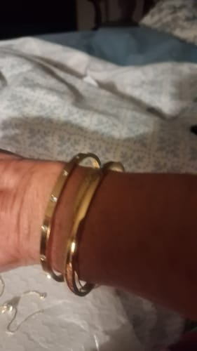 Customer's wrist wearing a gold Marbella Cuff Bracelet stacked with another thin bracelet.