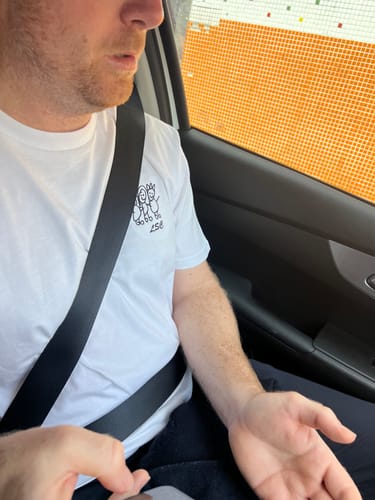 Customer's Customisation white t-shirt featuring a simple black line-art embroidery, worn while seated in a car.