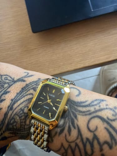 Customer's gold and silver Claire De Mains watch with a black face, worn on a tattooed wrist.