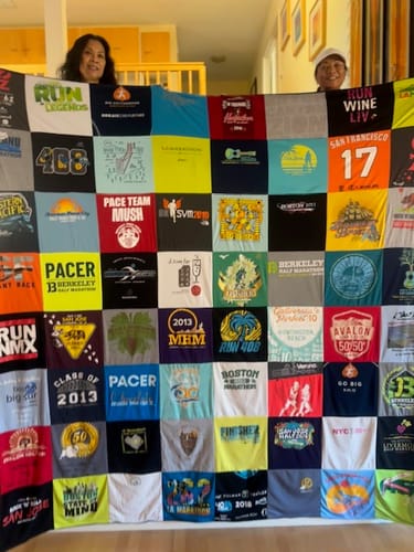 Customer's Project Repat T-Shirt Quilt held up by two people, displaying a grid of colorful, assorted athletic shirts.