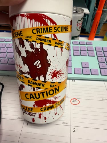 Customer's Universal Buddy cup with a white base and crime scene tape graphic, sitting on a desk.
