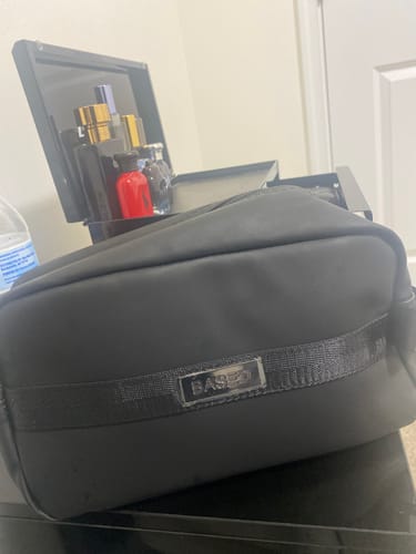 Customer's black Toiletry Bag sitting on a surface with various cologne bottles in the background.