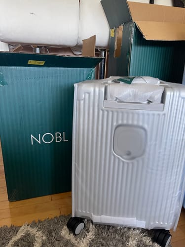Customer's new white suitcase with ridges, shown in front of its branded shipping box.