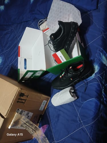 Customer's Mazerata Pigale 5 Sneakers in black, displayed inside their open shoe box on a blue bedspread.