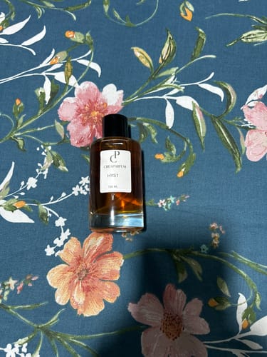 Customer's HYS1 fragrance bottle with amber liquid, resting on a floral print fabric background.