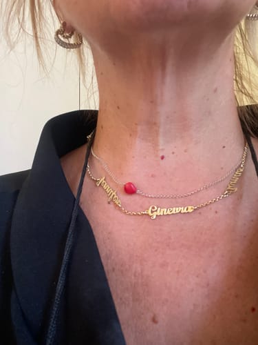 Customer's Collana Nomi in Corsivo in oro indossata al collo insieme a un'altra collana con una pietra rossa.