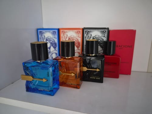 Customer's Kit Adonis e Attracione Men, quatro frascos de perfume coloridos com caixas correspondentes sobre mesa.