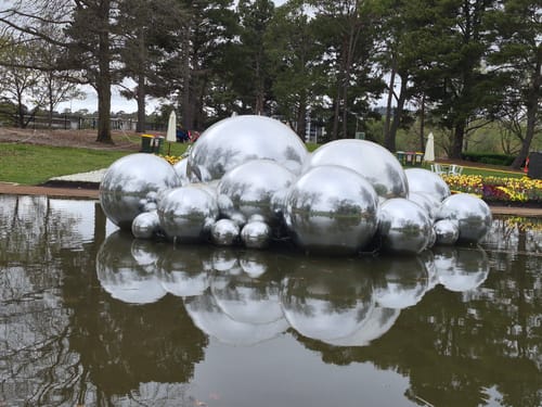 Customer's outdoor view of reflective spherical sculptures near water, reflecting a park setting.