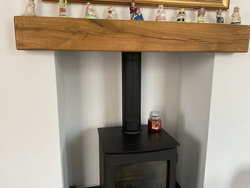 Customer's Rustic Oak Fireplace Beam installed above a wood burner with ornaments on the shelf.