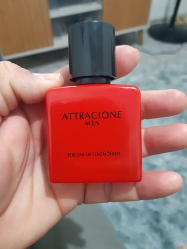 Customer's hand holding the bright red Attracione Men pheromone perfume bottle