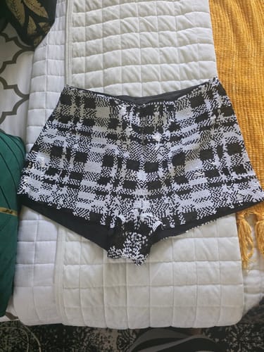 Reviewer's sequin plaid hot pants laid flat on a white quilted blanket.